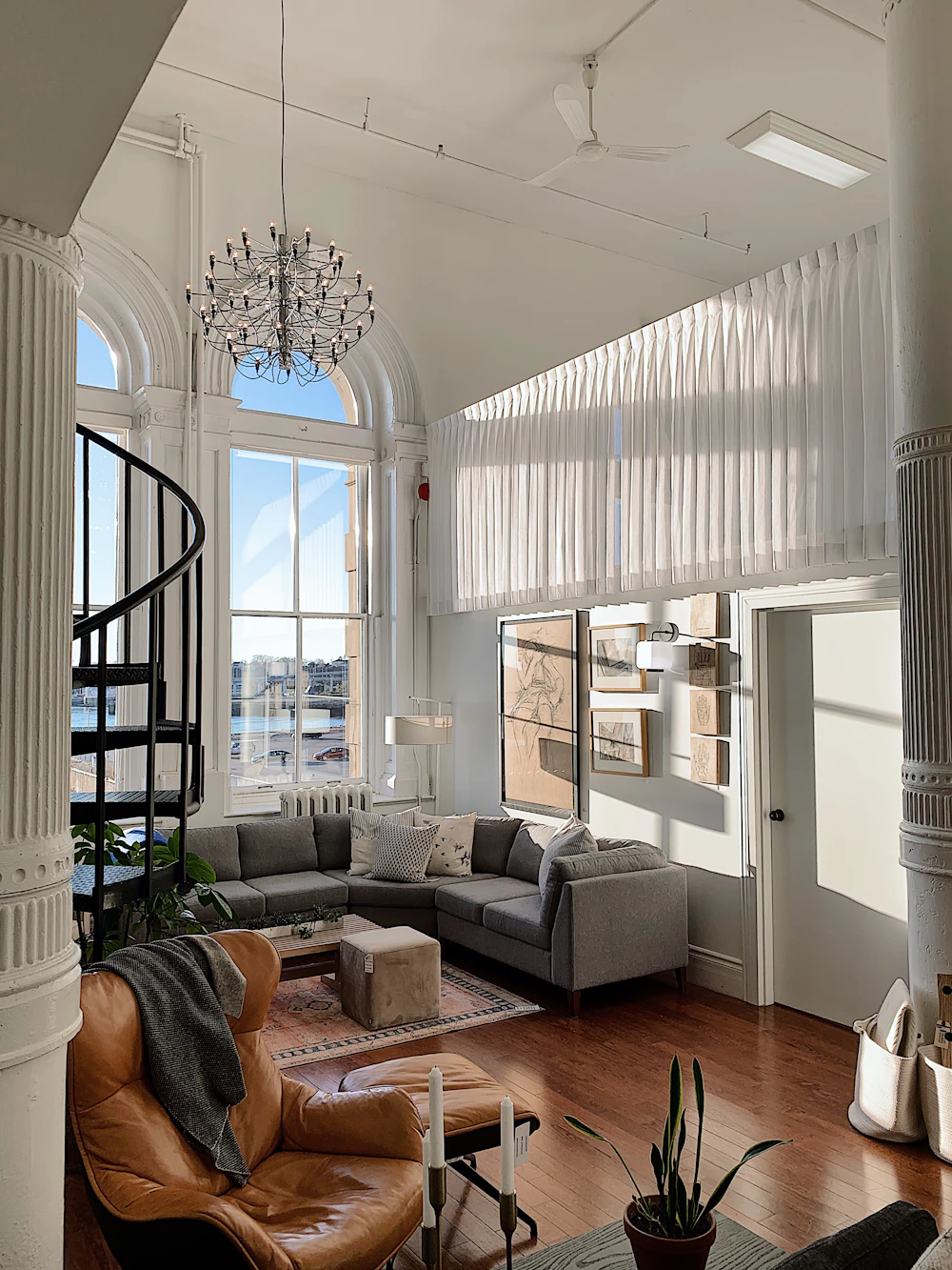 Bright loft living room with tall windows, a spiral staircase and a gray sofa